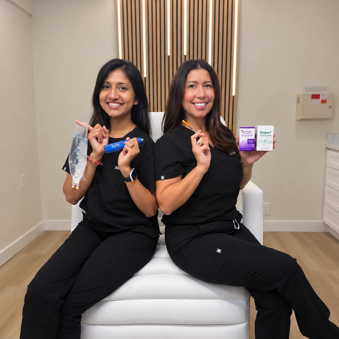 Ria Jivan, BSN, RN holding an IV hydration bag, seated with Kia Brooks, RN